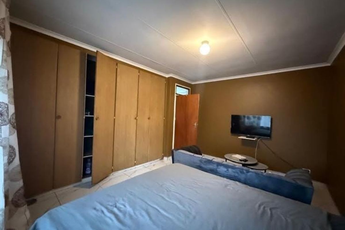 A bedroom featuring built-in wooden cupboards, tiled flooring, and neutral wall tones, offering a functional space with potential for modern updates.