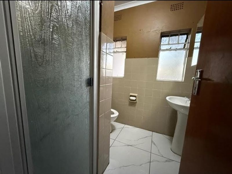A functional bathroom featuring a pedestal basin, toilet, and shower enclosure with tiled finishes, offering potential for modernization and aesthetic updates.