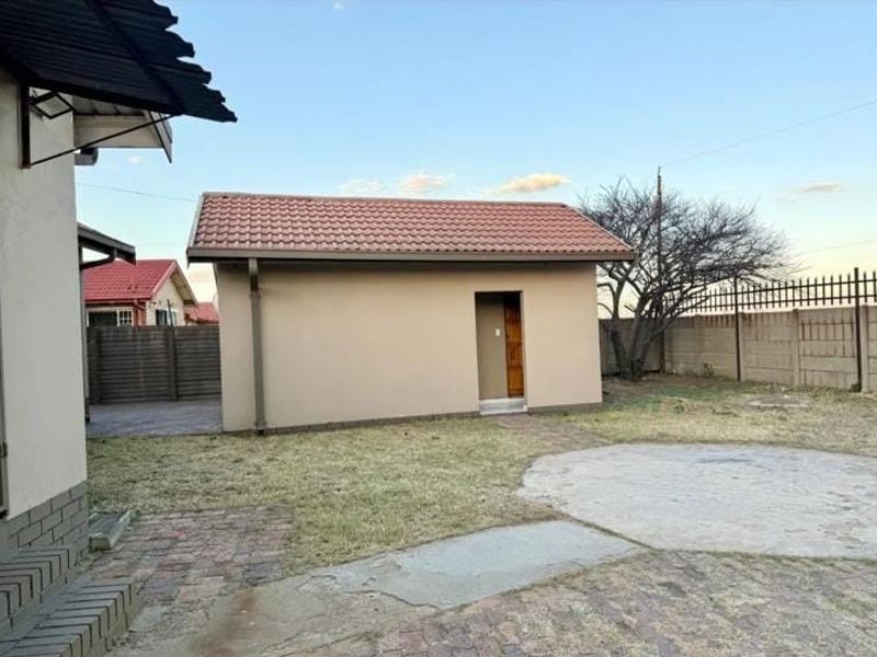 Rear garden view featuring a detached outbuilding with a tiled roof, concrete paving, and perimeter boundary walling.