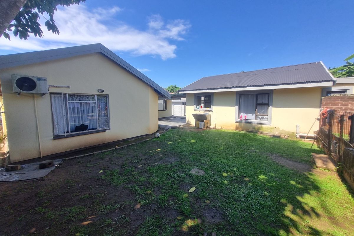 Rear view of the property showing a grassy yard area between two building sections with an external utility sink and security window bars.