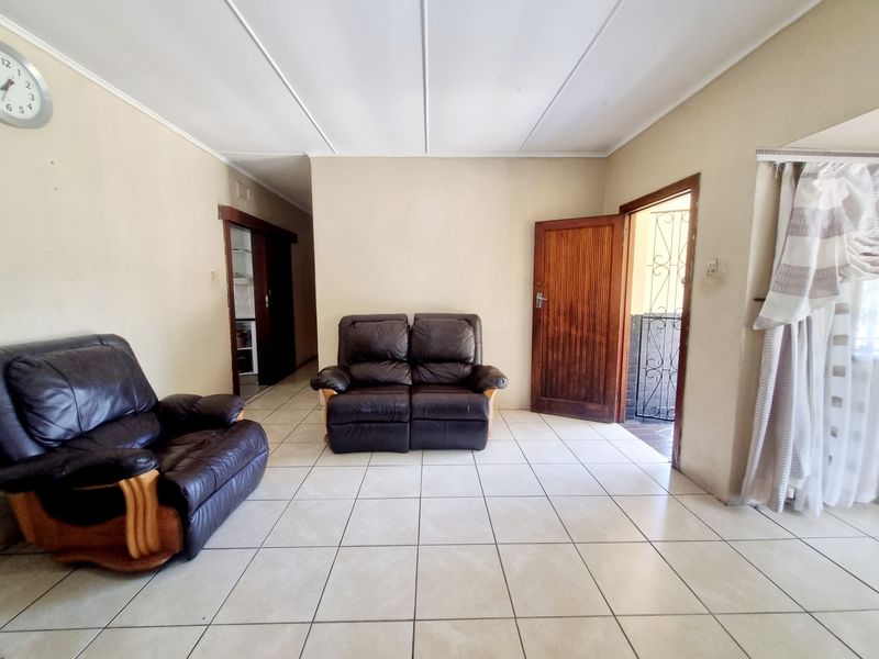 A living room featuring tiled flooring and a wooden entrance door, leading to an adjacent hallway and exterior access.