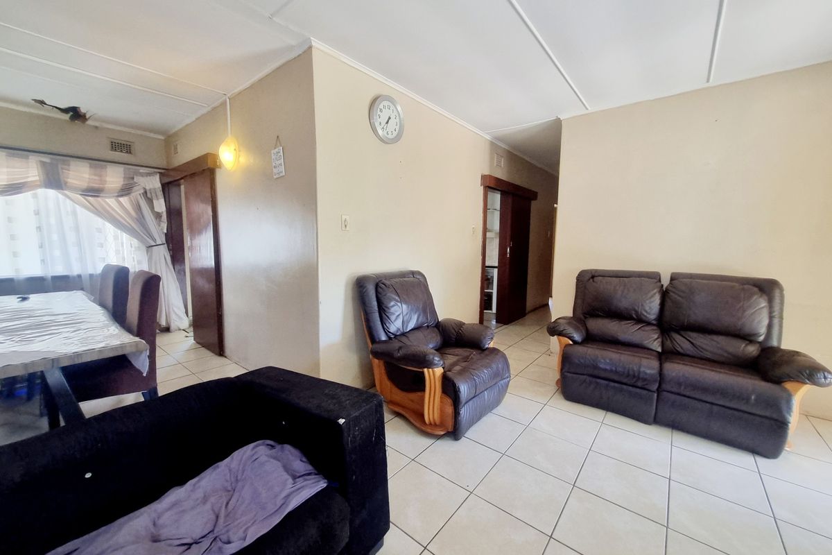 A spacious living area featuring tiled flooring and neutral wall tones, providing a functional layout with access to adjacent rooms.