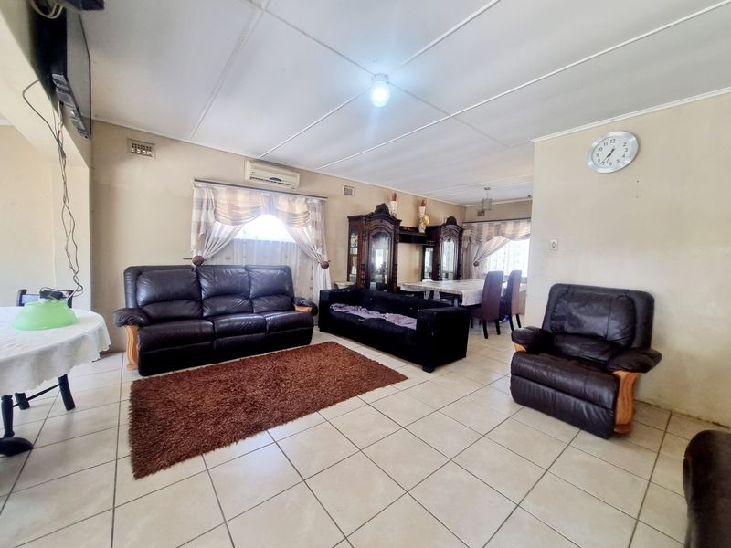 Spacious open-plan living and dining area featuring tiled flooring, ceiling panels, and a wall-mounted air conditioning unit.