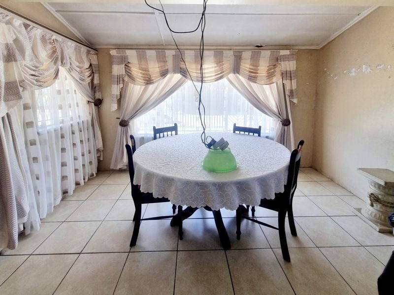 Dining room featuring tiled flooring and large windows, currently requiring cosmetic updates to the wall finishes and electrical fixtures.