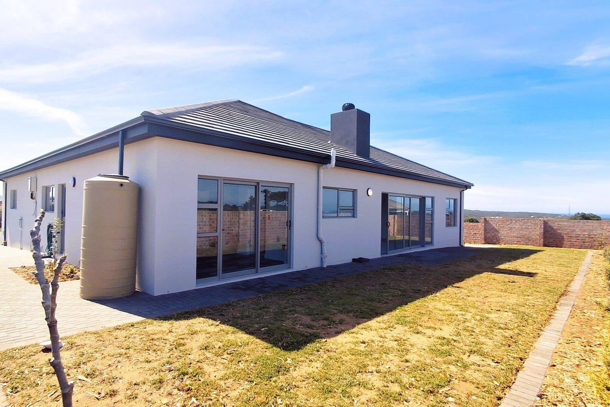 Rear view of a modern house featuring a paved patio, water tank, sliding glass doors, and a brick boundary wall.