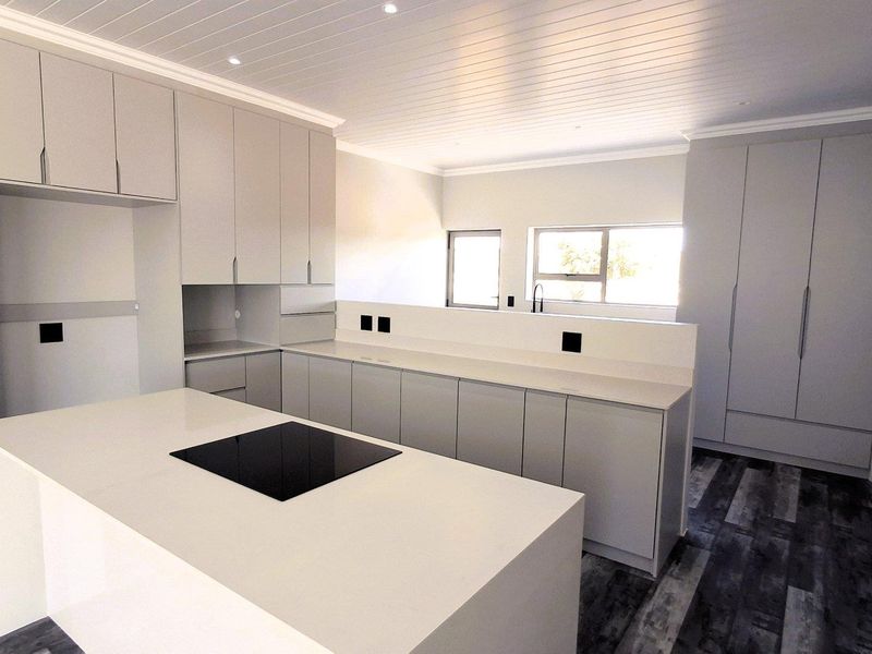 Modern, newly renovated kitchen featuring sleek grey cabinetry, stone countertops, a central island with an integrated cooktop, and stylish wood-look flooring.