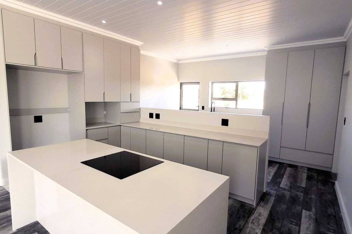 Modern, newly renovated kitchen featuring sleek grey cabinetry, stone countertops, a central island with an integrated cooktop, and stylish wood-look flooring.