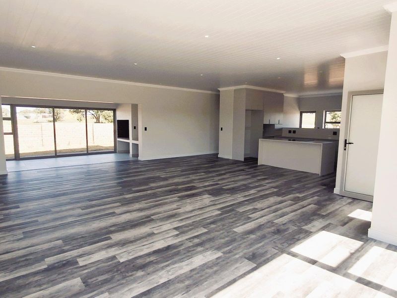 Spacious open-plan living area featuring modern laminate flooring, recessed lighting, and a sleek kitchen with a central island, flowing out to a patio.
