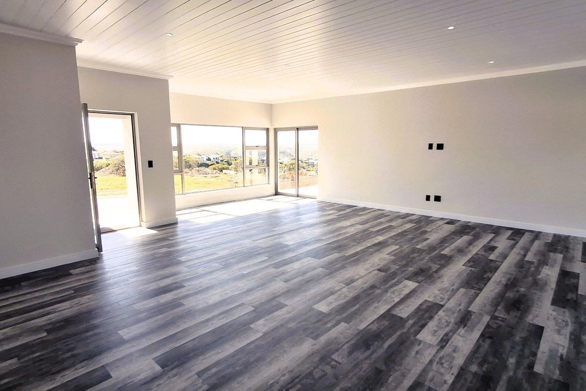 A spacious, light-filled living area featuring modern laminate flooring, a white tongue and groove ceiling, and large aluminium windows with scenic views.