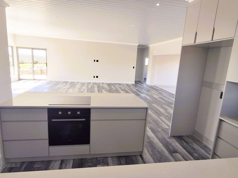 Spacious open-plan living area featuring a modern kitchen island with built-in oven and hob, complemented by contemporary laminate flooring and neutral finishes.
