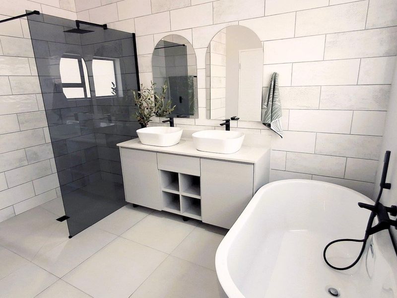 Modern bathroom featuring a double vanity with vessel sinks, a freestanding bathtub, and a spacious walk-in shower with contemporary black fixtures and subway tiling.