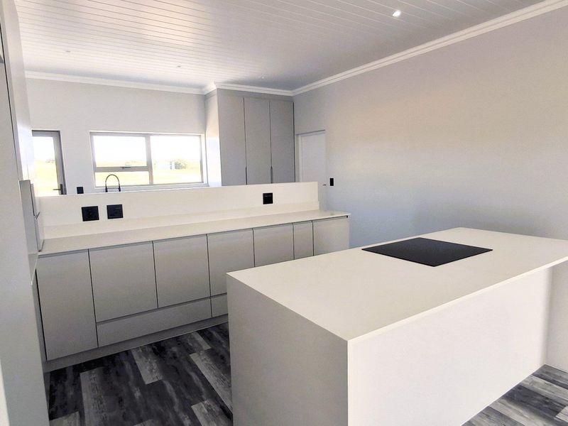 Modern, minimalist kitchen featuring a central island with an integrated cooktop, sleek cabinetry, stone countertops, and a bright, clean aesthetic.