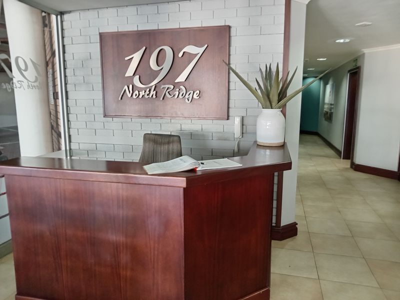 Professional office building entrance featuring a reception desk, brick feature wall with signage, and tiled flooring leading into a hallway.