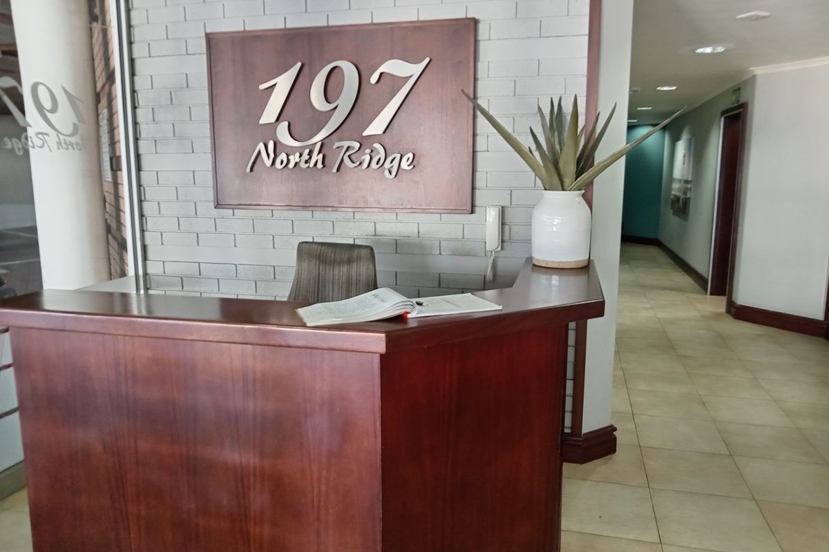 Professional office building entrance featuring a reception desk, brick feature wall with signage, and tiled flooring leading into a hallway.