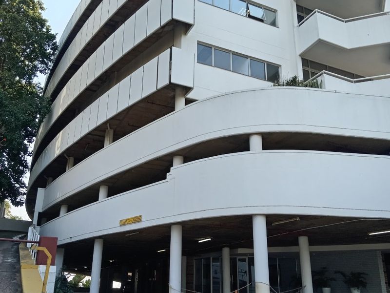Exterior view of a multi-story office building featuring a curved facade, concrete structural columns, and a paved ground-level parking area.