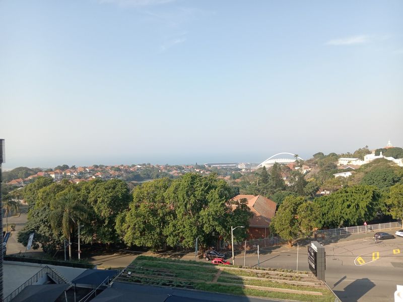 Elevated panoramic view overlooking the surrounding neighbourhood, lush greenery, and distant coastal landscape.