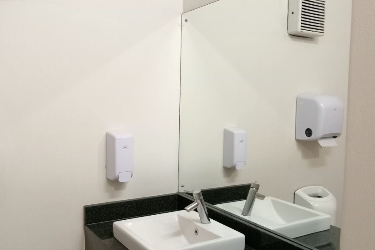 A clean, modern office restroom vanity area featuring a granite countertop, integrated ceramic basin, and wall-mounted mirror with essential utility dispensers.