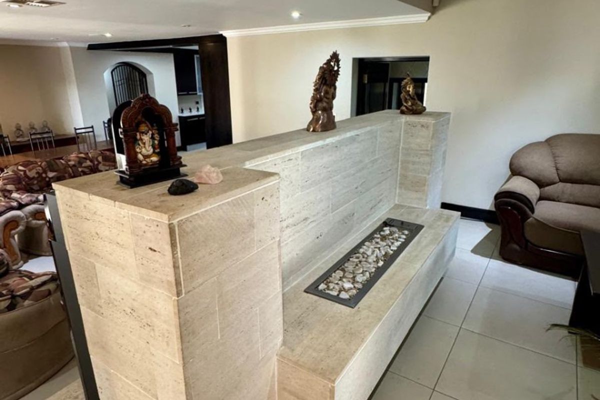 Spacious living area featuring a custom travertine stone partition wall with a built-in bench and decorative pebble inlay, complemented by neutral tiled flooring.