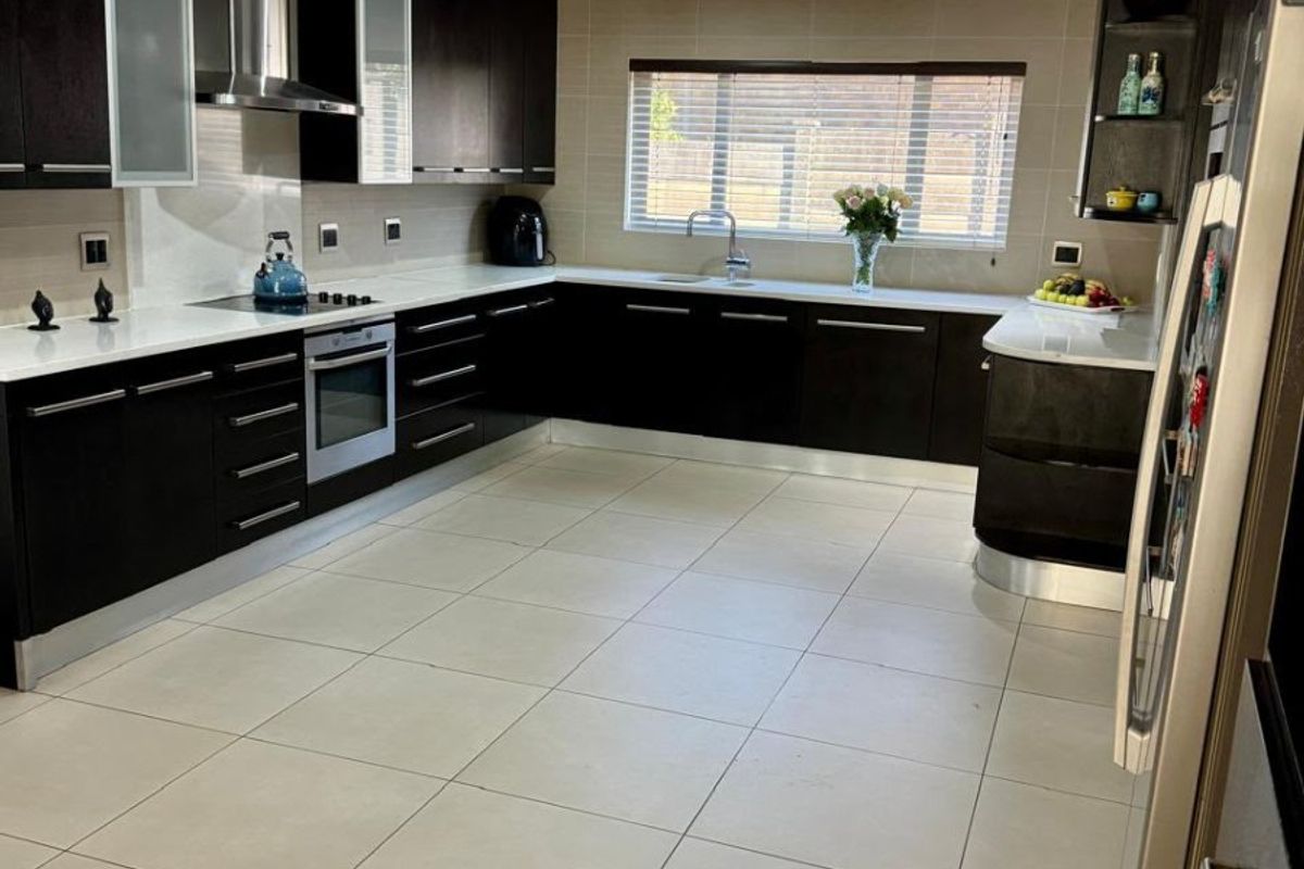 A modern, spacious kitchen featuring dark cabinetry, stone countertops, integrated stainless steel appliances, and large format floor tiles.