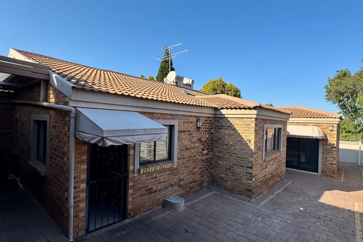 Rear exterior view of a face brick house featuring a paved courtyard, tiled roof, and window awnings.