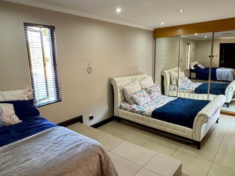 Spacious bedroom featuring large built-in mirrored wardrobes, tiled flooring, and recessed lighting, offering a clean and functional living space.