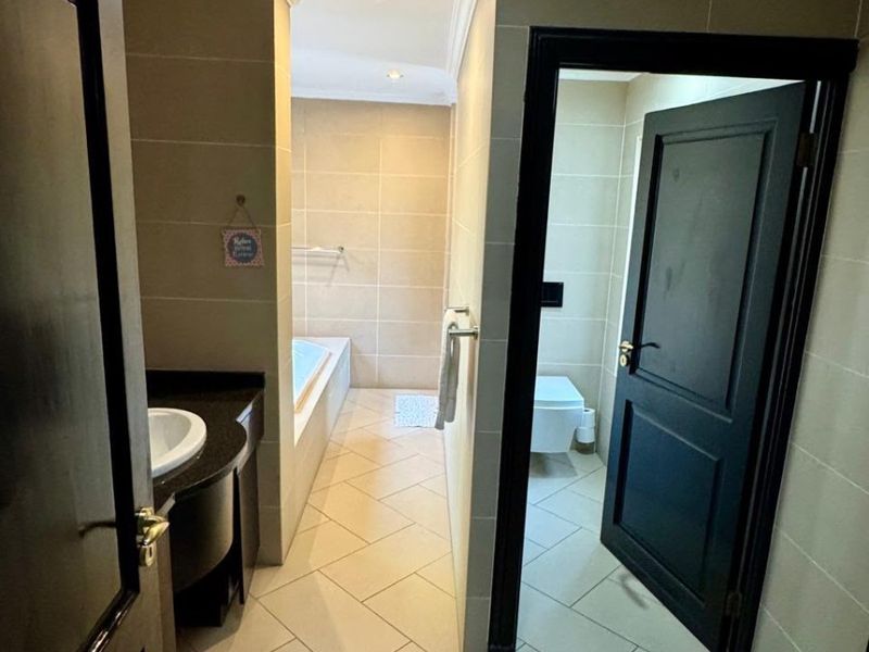 A modern bathroom featuring a built-in vanity with an undermount sink, a tiled bathtub, and a separate enclosed toilet area with neutral tiling.