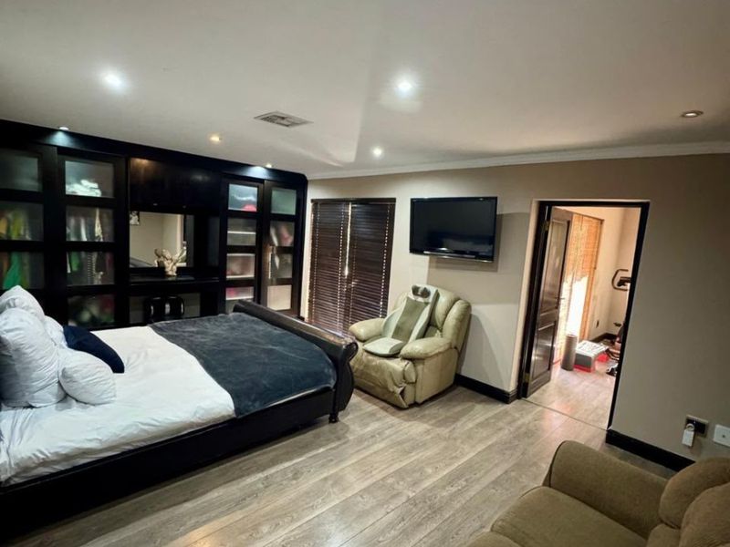 Spacious bedroom featuring extensive built-in cabinetry, modern laminate flooring, recessed lighting, and direct access to an adjoining room.
