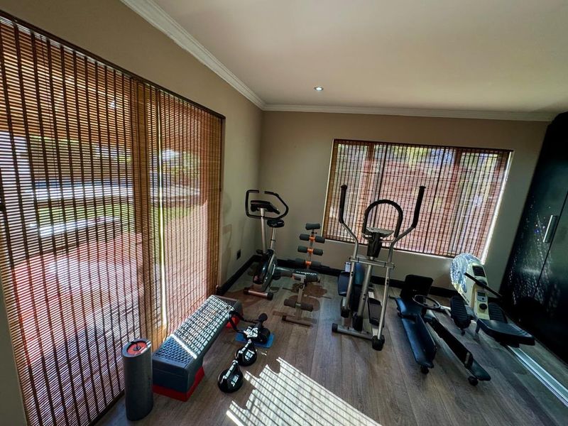 A dedicated home gym space featuring laminate flooring, recessed lighting, and large windows with fitted blinds, providing a functional area for fitness activities.