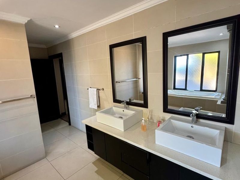 Modern bathroom featuring a double vanity with vessel sinks, framed mirrors, tiled walls and floors, and a built-in bathtub.