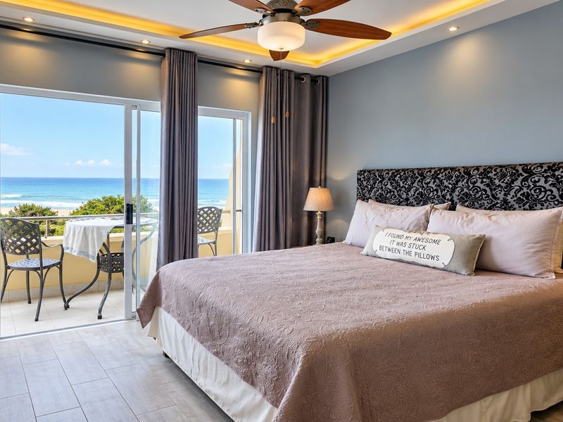 Spacious bedroom featuring modern tiled flooring, recessed ceiling lighting, a ceiling fan, and sliding glass doors opening onto a private balcony with ocean views.