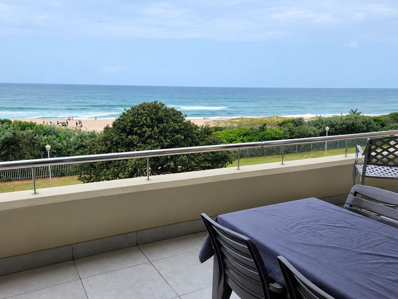 A spacious balcony featuring a stainless steel balustrade and tiled flooring, offering an expansive, unobstructed view of the ocean and beach.