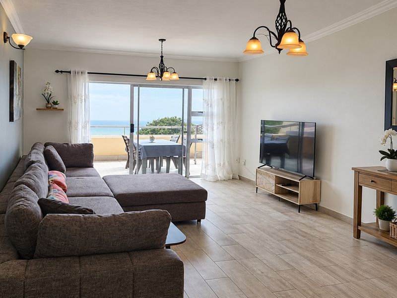 Spacious living room featuring tiled flooring, coving, and large sliding glass doors that open onto a balcony with ocean views.