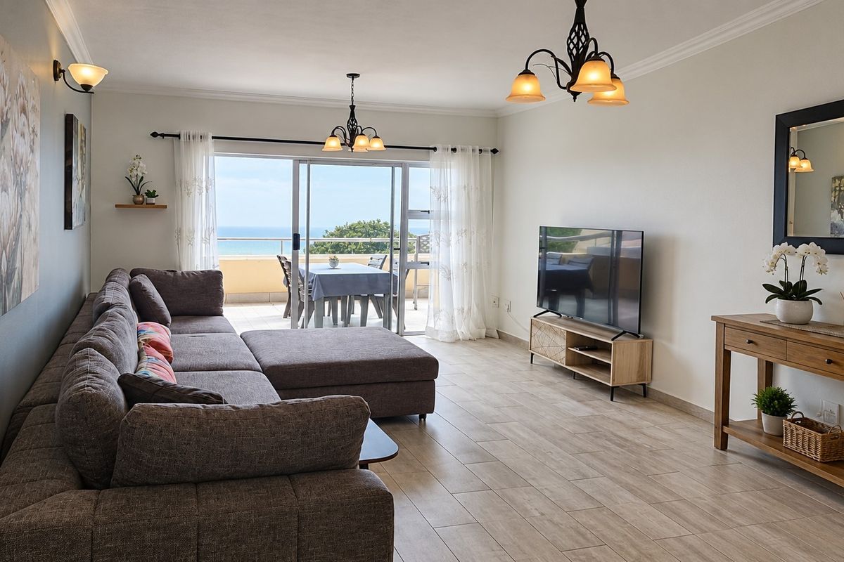 Spacious living room featuring tiled flooring, coving, and large sliding glass doors that open onto a balcony with ocean views.