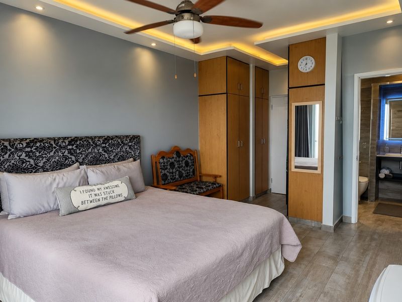 A well-maintained bedroom featuring built-in wooden cupboards, recessed ceiling lighting, a ceiling fan, and direct access to an en-suite bathroom.