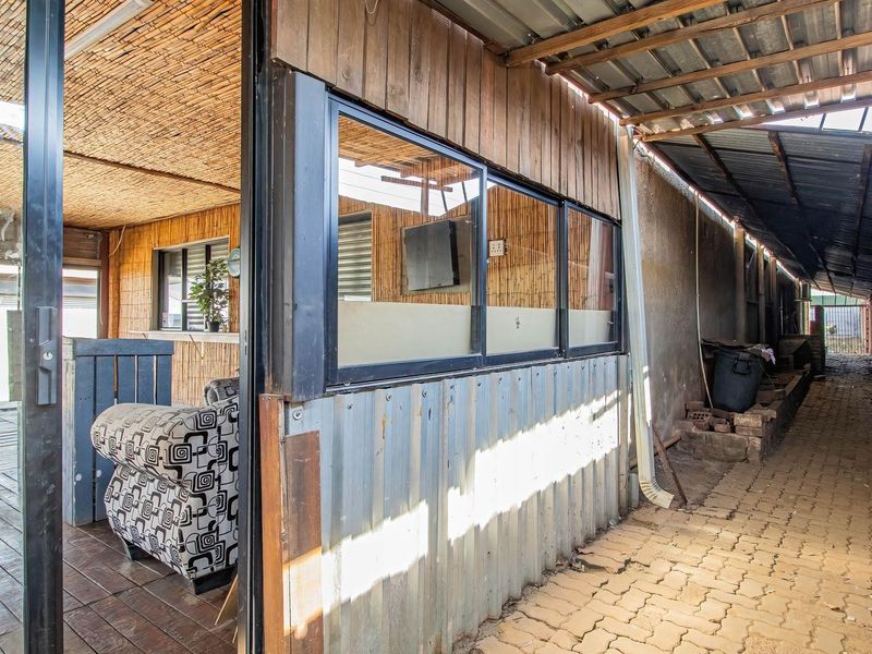 A covered outdoor patio area featuring corrugated metal and timber finishes, adjacent to a paved side walkway with metal roofing.