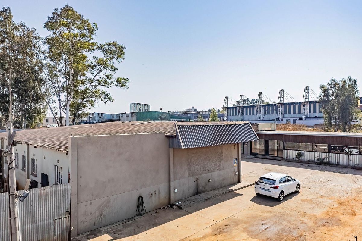 Aerial view of the rear exterior of a commercial property featuring a large concrete building, corrugated metal roofing, and a paved yard area.