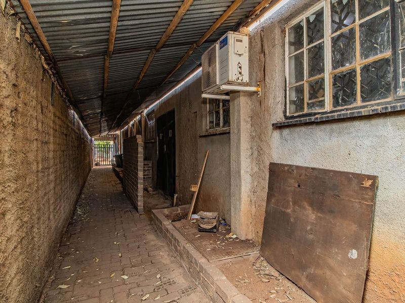 A narrow, covered exterior service alleyway featuring a paved walkway, brick walls, and an external air conditioning unit.