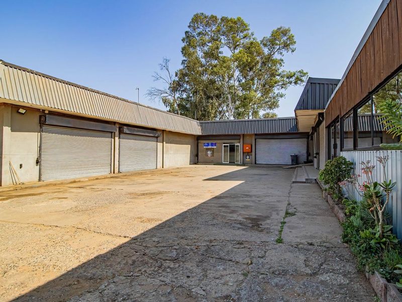 Rear exterior yard area featuring multiple roller shutter doors, concrete paving, and metal cladding, suitable for industrial or commercial storage access.
