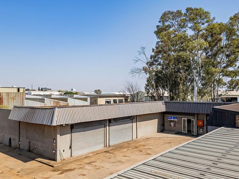 Aerial view of a commercial property featuring a concrete yard, multiple metal roller shutter doors, and corrugated metal roofing.
