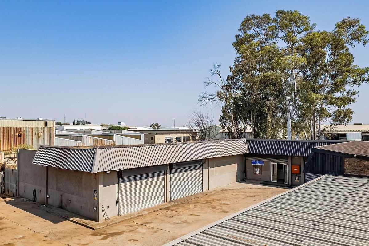 Aerial view of a commercial property featuring a concrete yard, multiple metal roller shutter doors, and corrugated metal roofing.