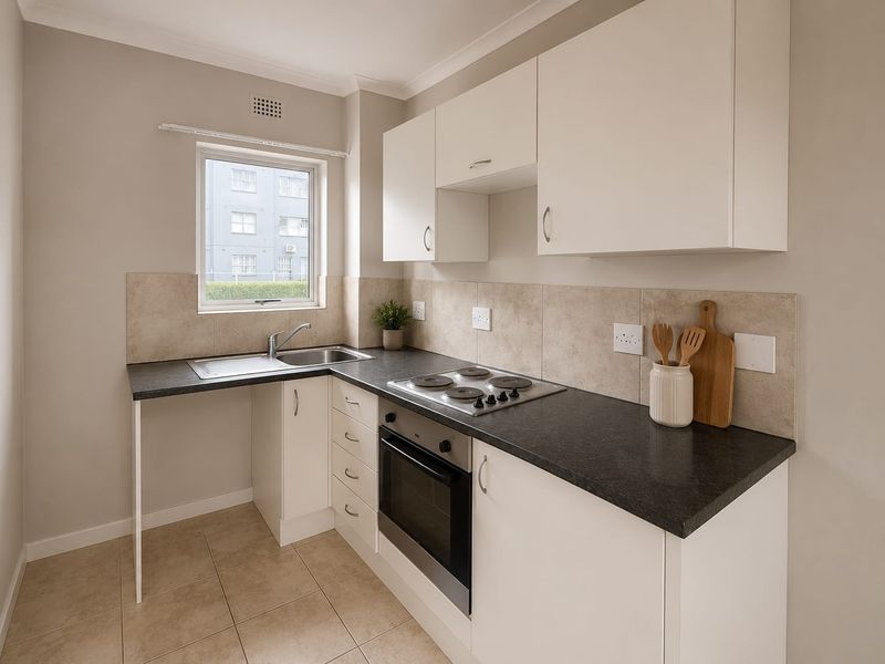 A clean and functional kitchen featuring white cabinetry, dark laminate countertops, a built-in oven, electric hob, and neutral tiled flooring.