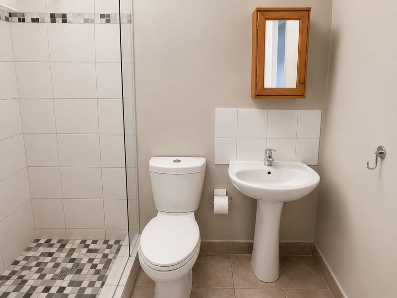 A clean, functional bathroom featuring a pedestal basin, a modern toilet, and a glass-enclosed shower with decorative tiled flooring.