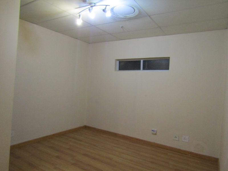 An empty bedroom featuring laminate flooring, a drop ceiling with recessed lighting, and a small high-set window.