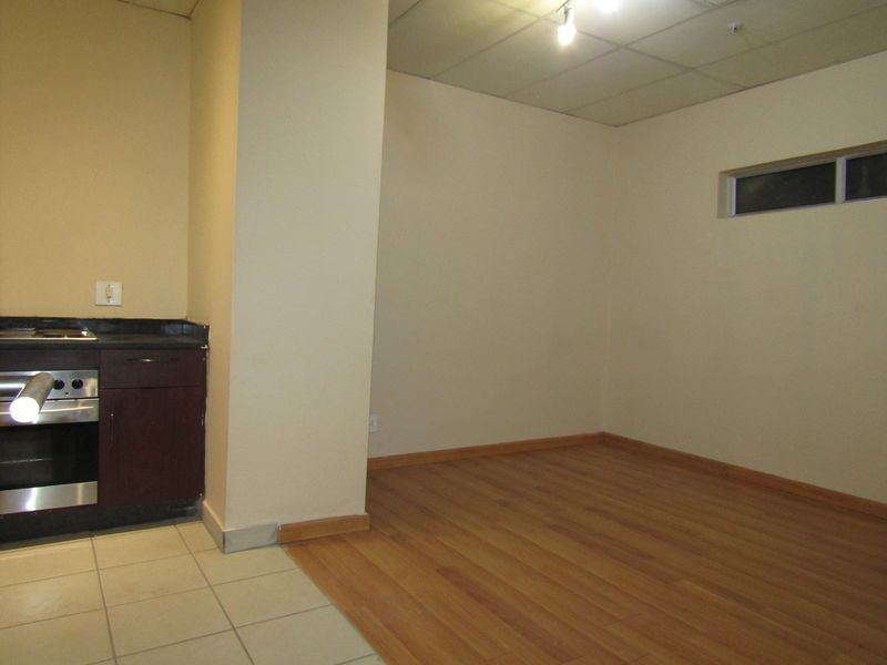 An empty open-plan living area featuring a compact kitchenette with built-in oven, hob, and stone countertops, finished with laminate and tiled flooring.