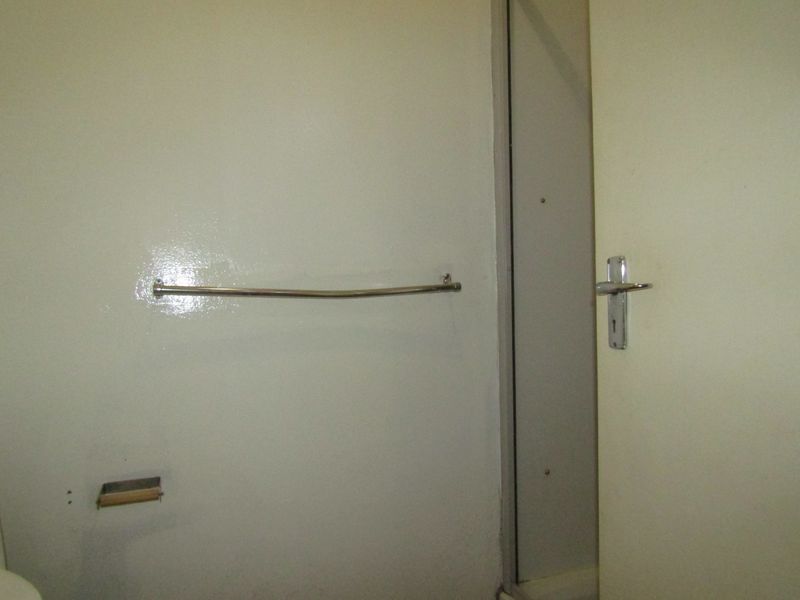 A view of a bathroom interior featuring a wall-mounted towel rail, toilet paper holder, and a door leading to a shower area.