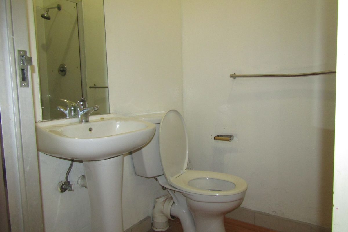 A compact bathroom featuring a pedestal basin, toilet, and shower area with basic fixtures, requiring cosmetic updates to improve its overall condition.