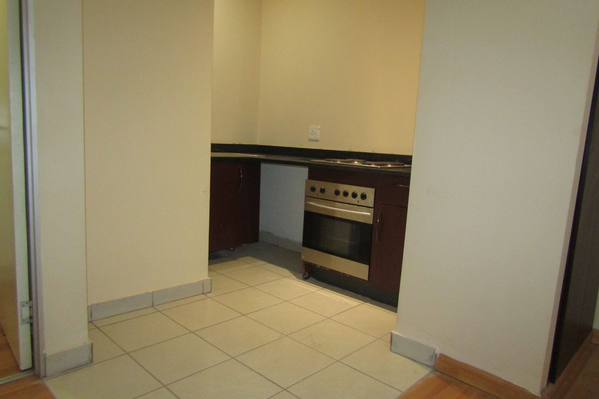 A compact kitchen area featuring built-in cabinetry, an oven, and hob, with tiled flooring and neutral walls, currently awaiting finishing touches.