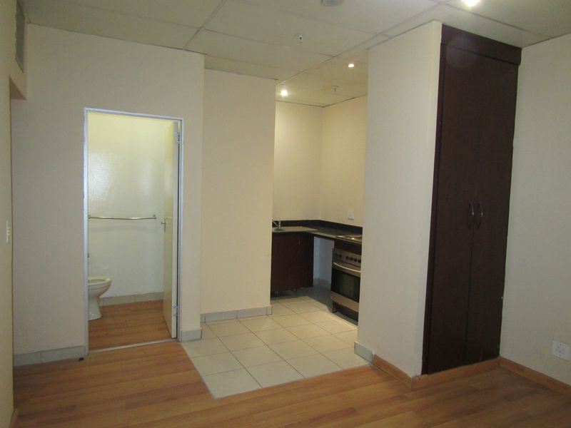 Open plan studio apartment featuring a compact kitchen with built-in oven and cabinetry, laminate flooring, and an adjacent bathroom.