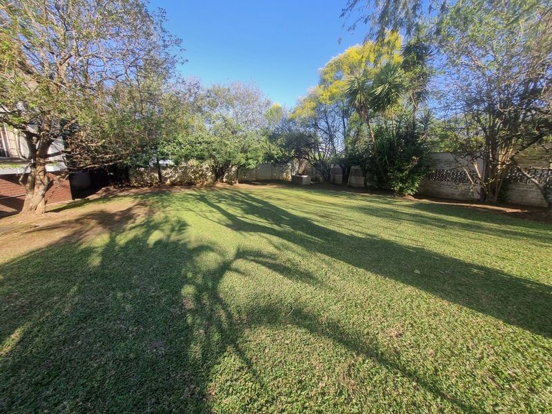A spacious, well-maintained private garden featuring a large lawn area surrounded by mature trees and a secure perimeter wall.