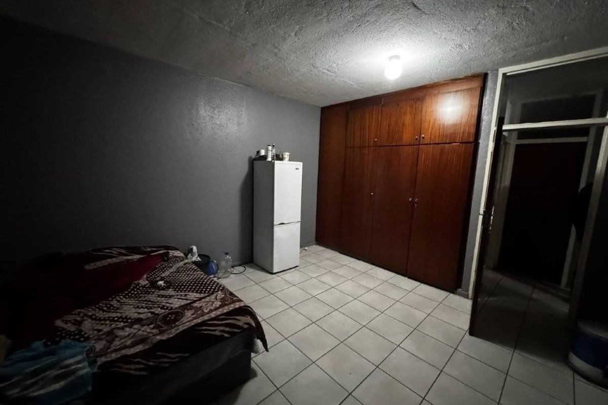 A bedroom featuring tiled flooring and a large built-in wooden wardrobe, requiring cosmetic updates to improve the overall aesthetic and lighting.